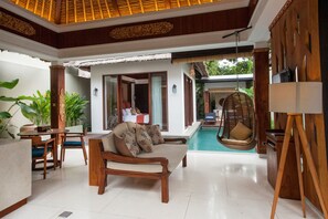 Un espacio interior amplio con piscina, muebles de madera y una silla colgante.