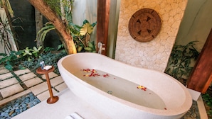 A stone bathtub with a wooden side table and a wall-mounted woven basket. - Regali Villa (Canggu)