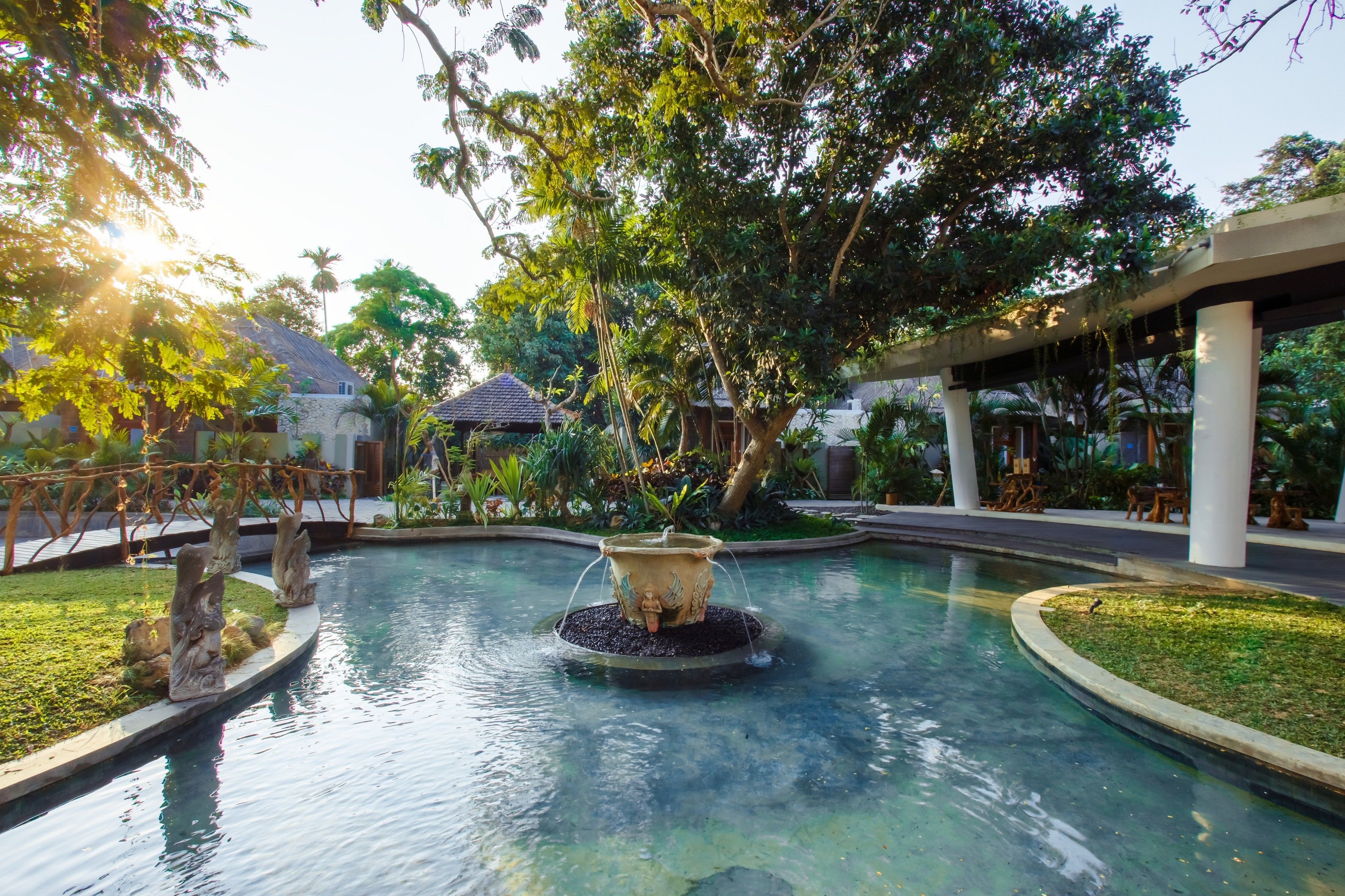 A serene pool area with a central fountain, surrounded by lush greenery and a covered seating area.