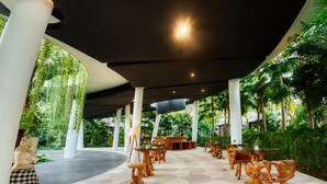 An outdoor seating area with round tables and chairs, surrounded by white columns and greenery. - Regali Villa (Canggu)