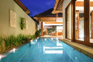Una piscina con techo de paja, zona de estar interior y paneles decorativos en la pared.