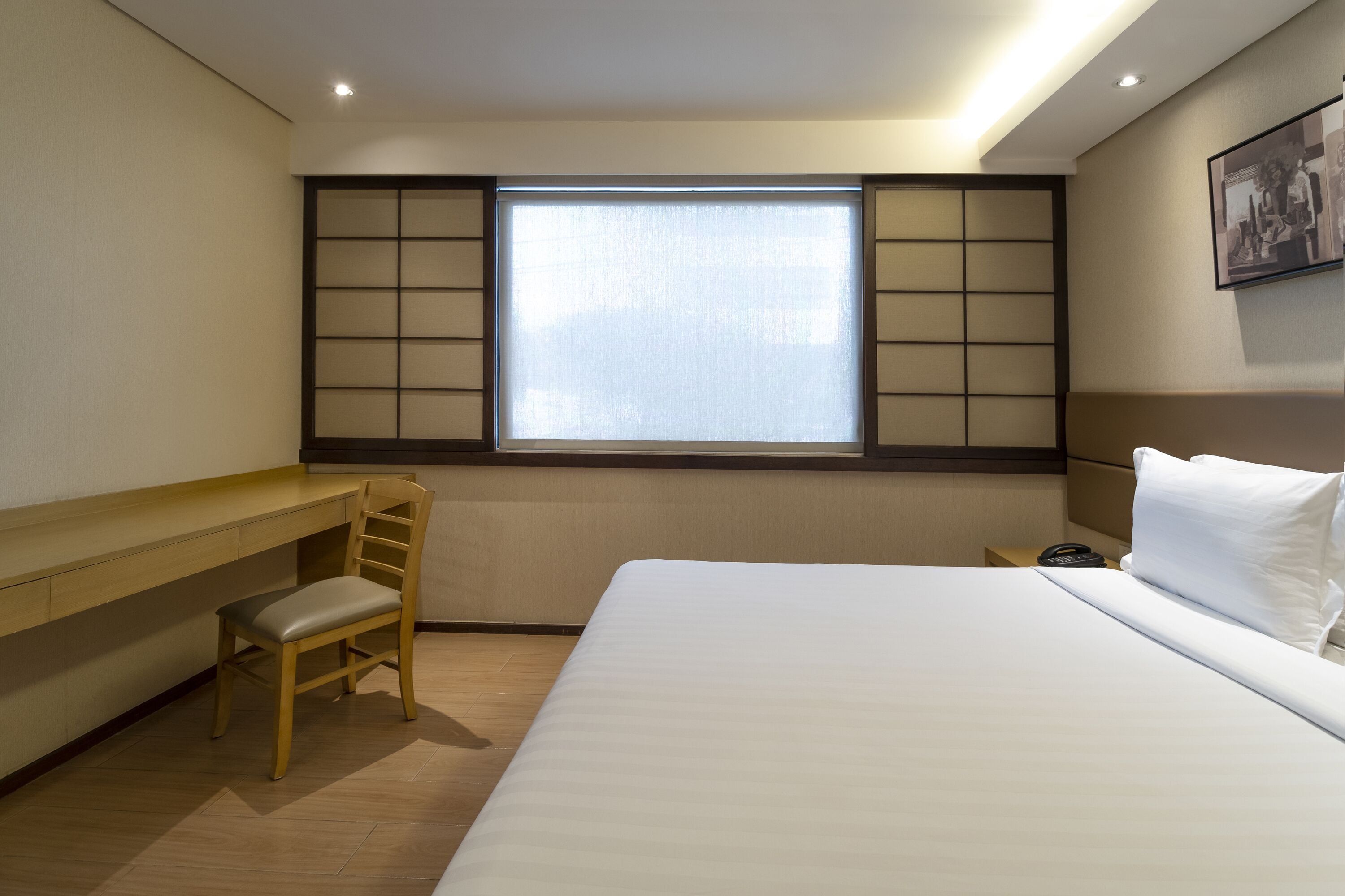 Una camera d'albergo con un letto, una scrivania con una sedia, una finestra con tende e un comodino con il telefono.