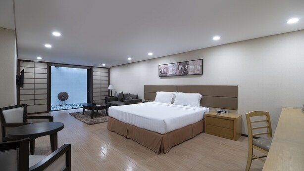 Una habitación de hotel moderna con una cama grande, un escritorio, una silla y vistas a través de un ventanal.
