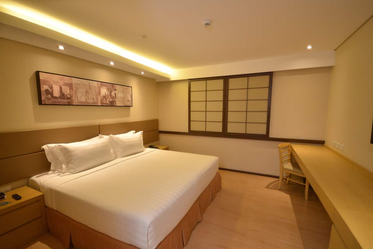 A hotel room with a large bed, a desk, a chair, a painting on the wall, and a window with a view.