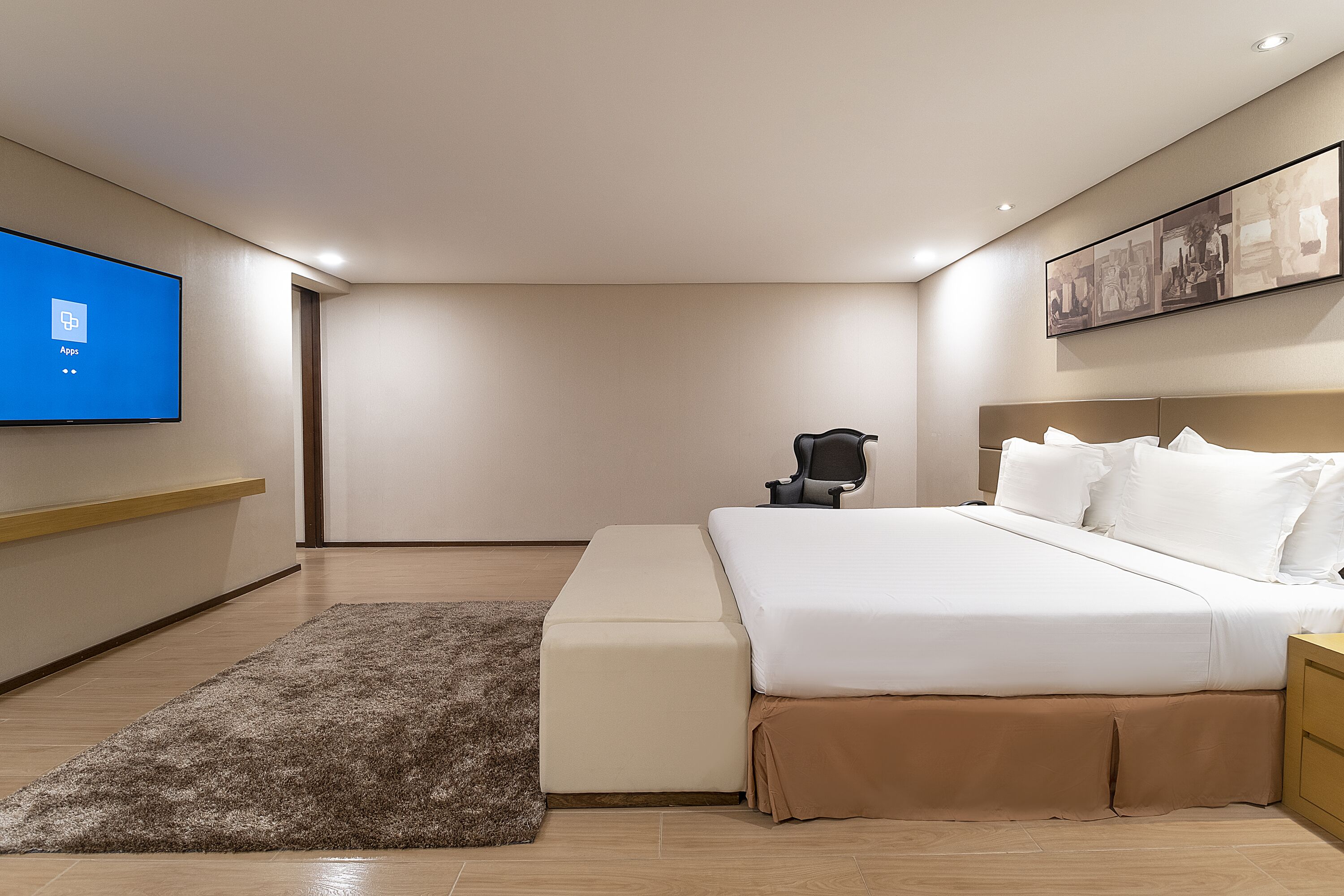 A modern bedroom with a bed, a TV mounted on the wall, a bedside table, and a chair.
