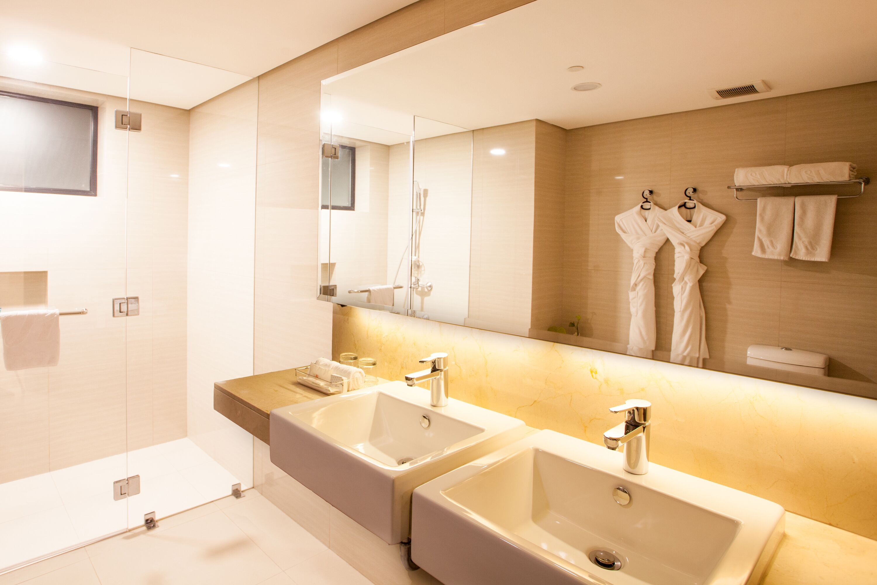 A modern bathroom with two sinks, a large mirror, and a glass shower enclosure.