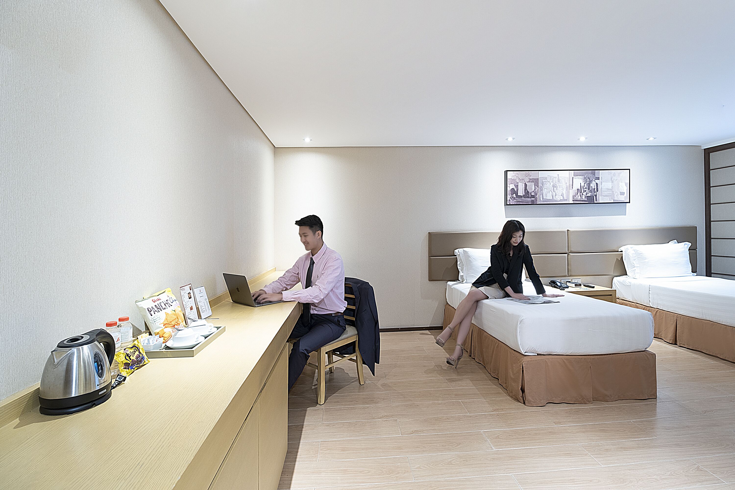 Habitación de hotel con escritorio, cama y sofá. Hay una tetera, una cafetera y una bolsa de aperitivos sobre el escritorio.