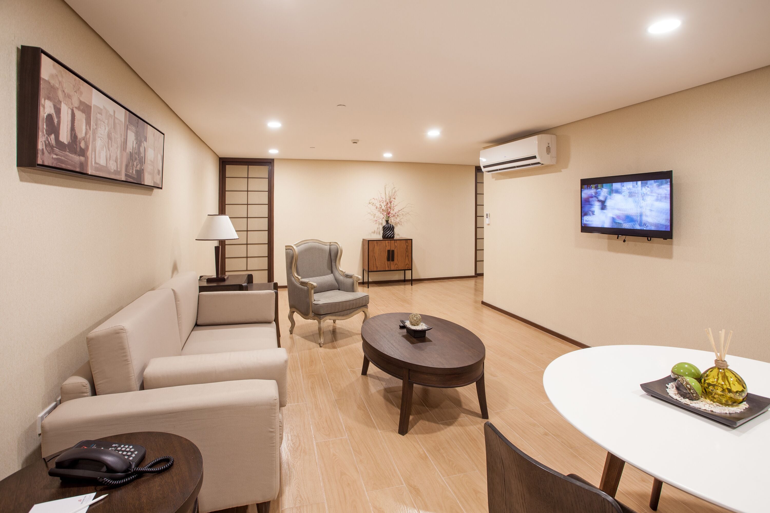 Habitación de hotel con sofá, sillón, mesa redonda y televisor montado en la pared.