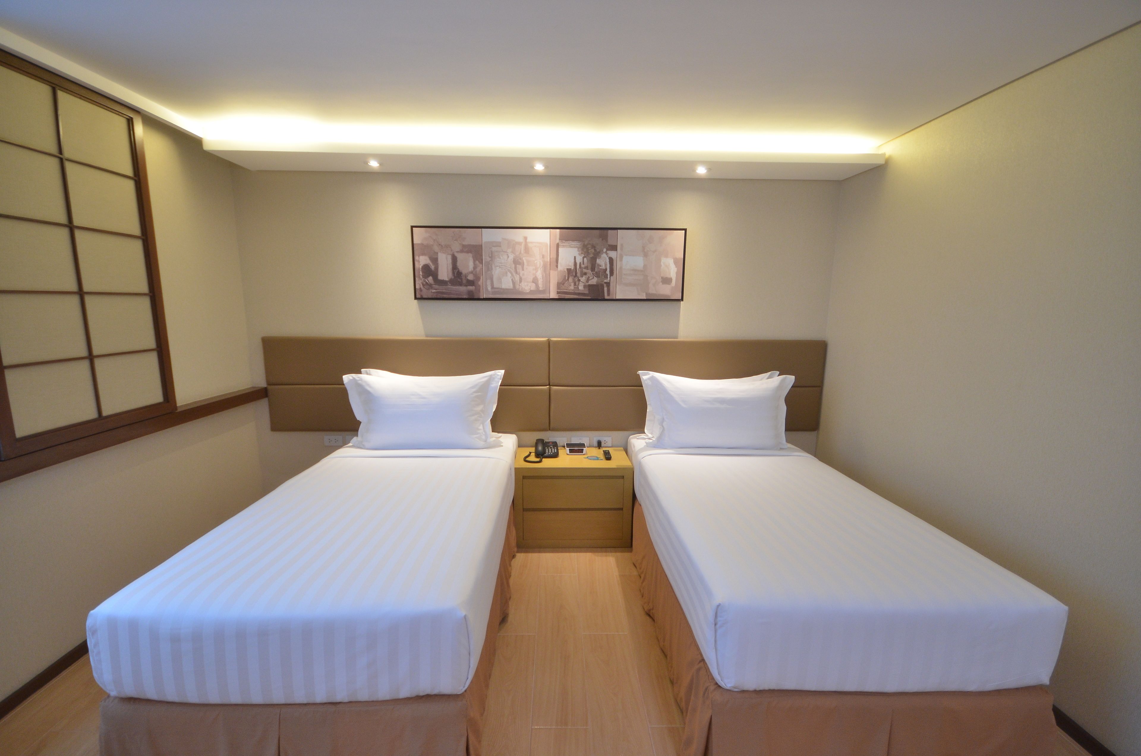 A hotel room with two single beds, a wooden nightstand, a framed picture on the wall, and a sliding door on the left.