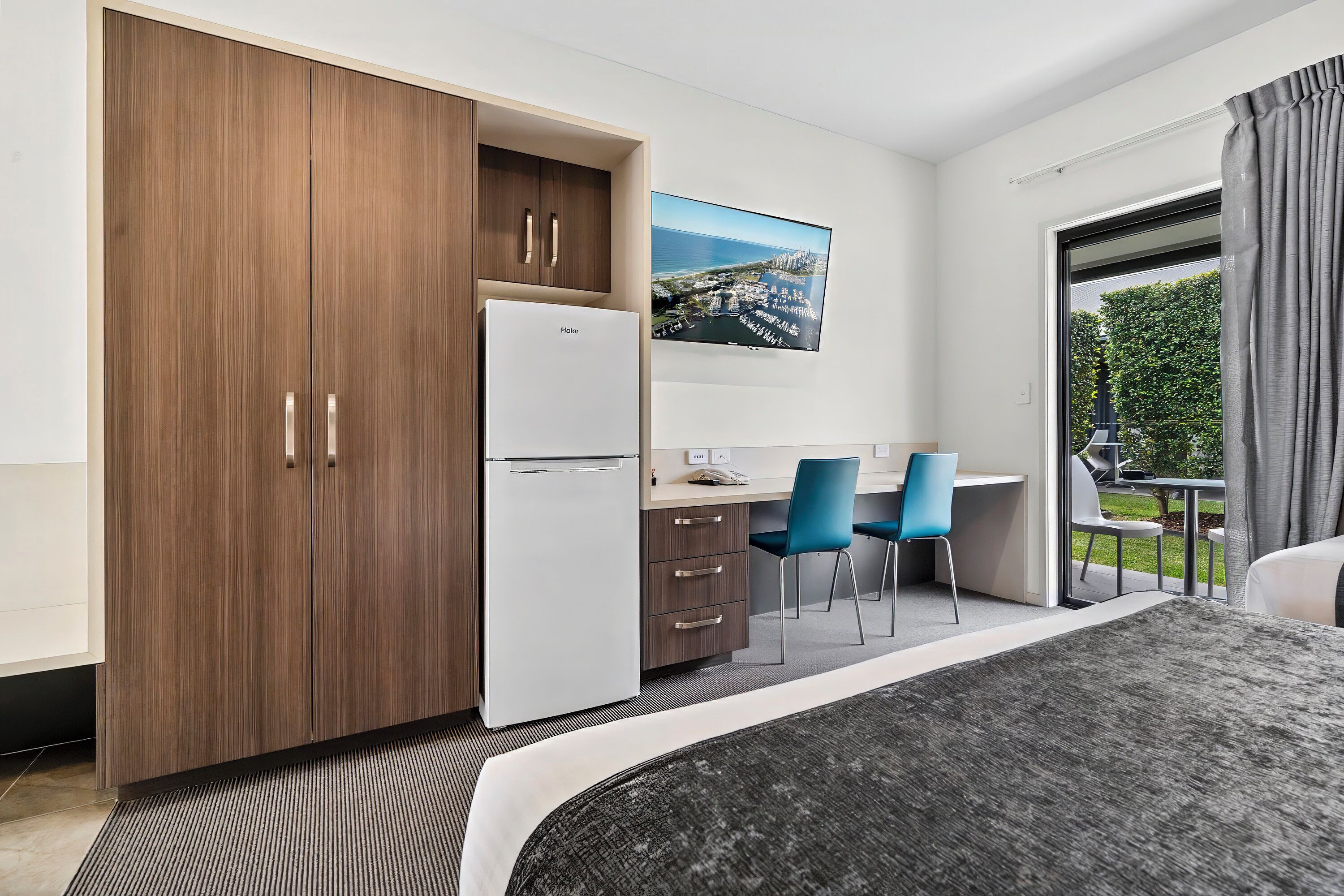 Habitación de hotel con cama, escritorio, dos sillas, refrigerador, armario y un gran ventanal con vistas.