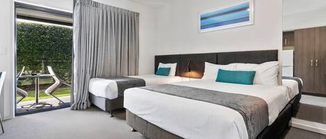 Habitación de hotel con una cama grande, un escritorio, una silla y vistas a un jardín a través de una puerta corredera.