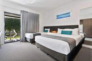 Habitación de hotel con una cama grande, un escritorio, una silla y vistas a un jardín a través de una puerta corredera.
