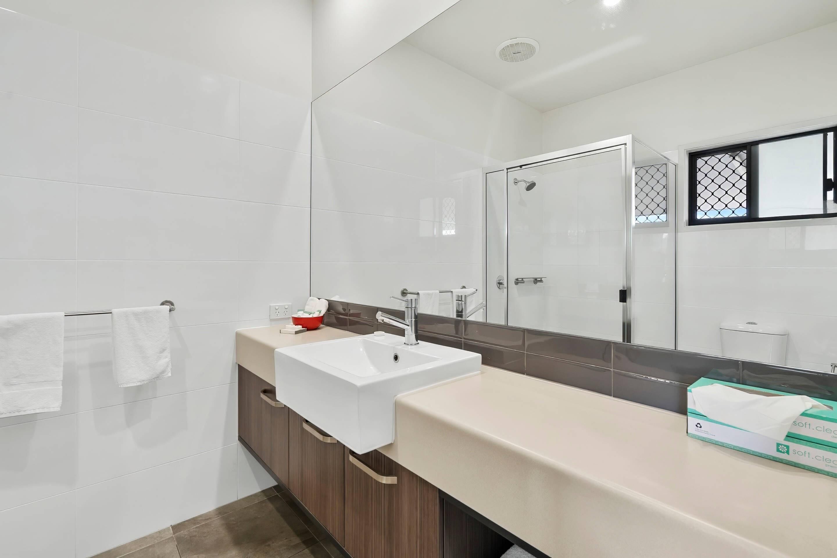 Un baño moderno con un lavabo blanco, cabina de ducha con mampara de vidrio y un espejo grande.