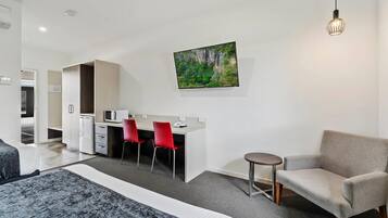 Una habitación de hotel moderna con una cama, un escritorio con dos sillas rojas, una mesita redonda y un cuadro de una cascada en la pared.