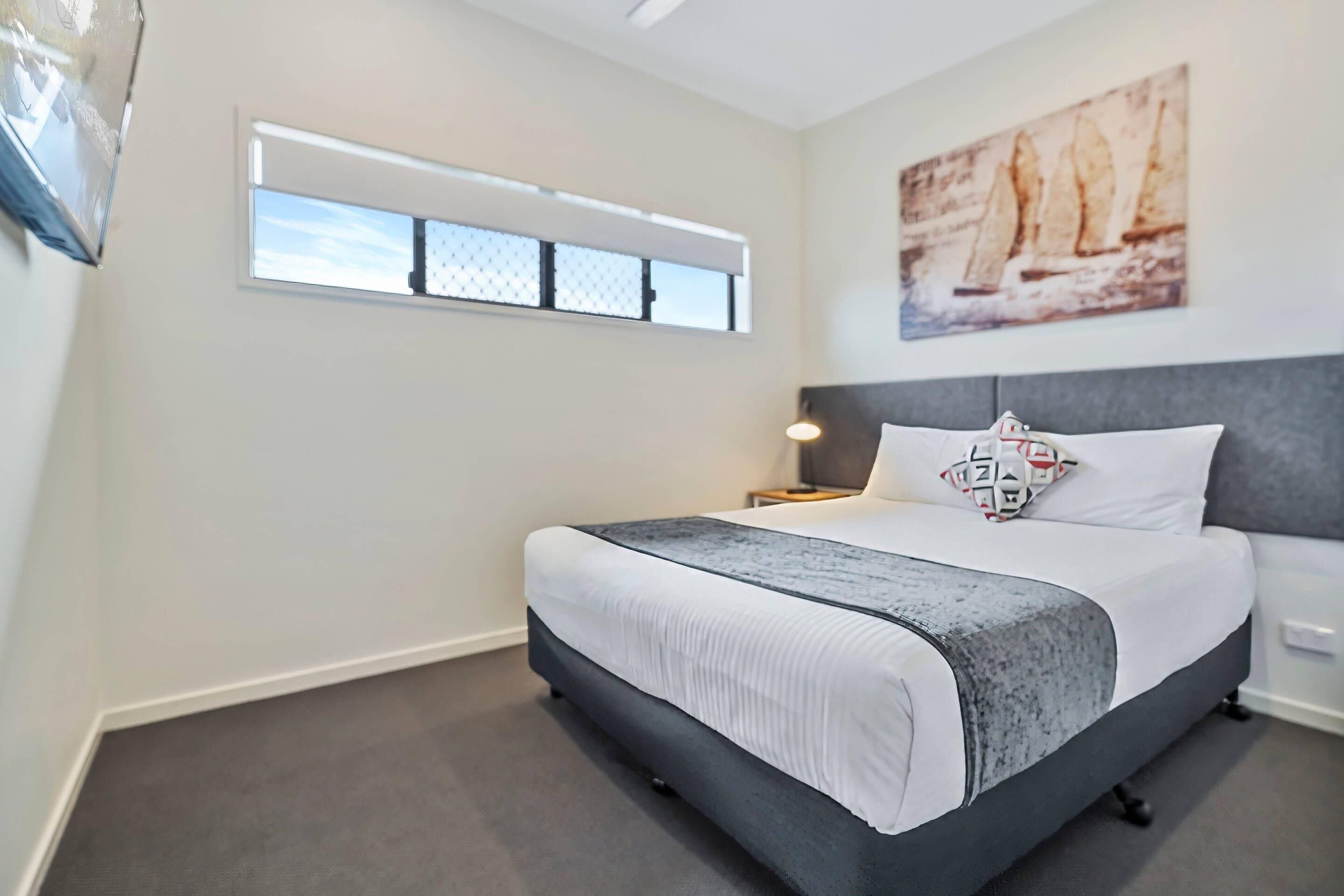 A bedroom with a bed, a window, a nightstand, a lamp, and a painting on the wall.