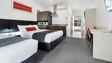 Quarto de hotel moderno com cama, mesas de cabeceira, escrivaninha e cozinha compacta.
