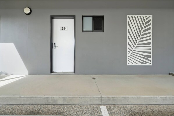 Entrada de un edificio con una puerta identificada con el número '314', un ventanal pequeño encima y un panel decorativo con diseño de hojas en la pared.