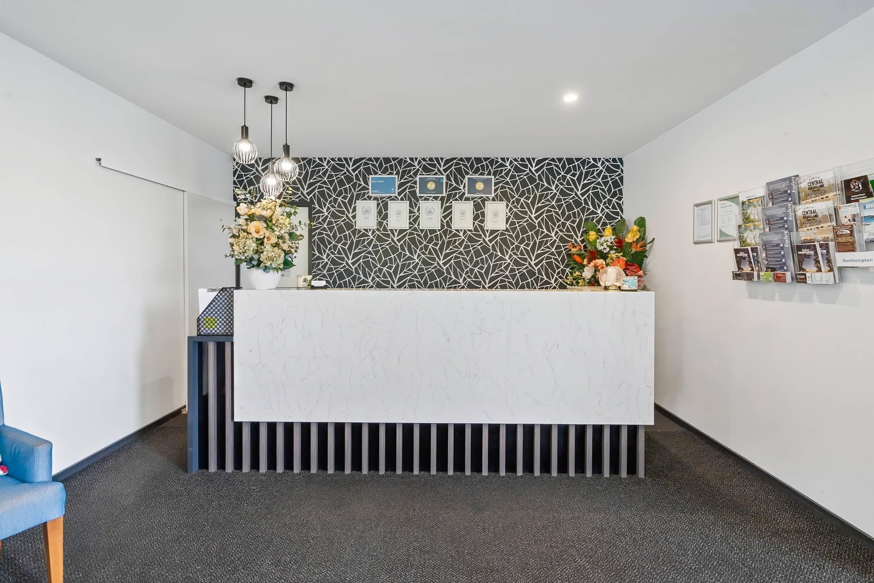 A reception desk with certificates, a flower arrangement, and a blue chair.
