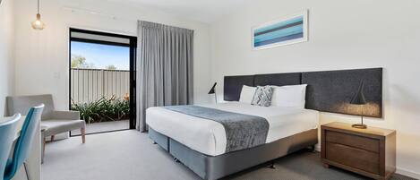A modern hotel room with a large bed, a bedside table with a lamp, a chair, and a view of the outdoors.