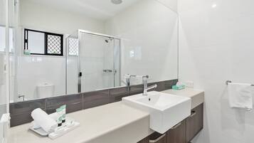 A modern bathroom with a large mirror, two sinks, a shower, and a towel rack.