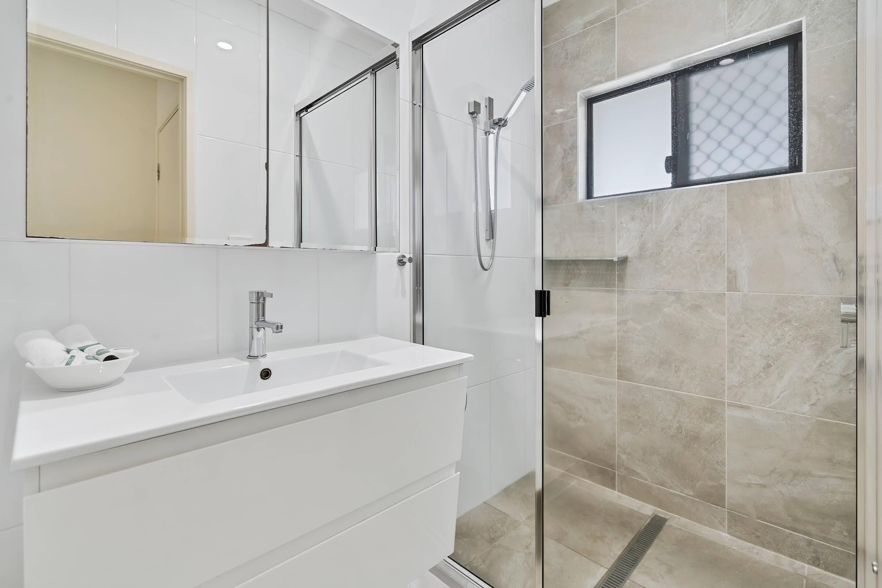 Un baño moderno con un lavamanos blanco, una cabina de ducha de vidrio y un revestimiento de mármol en la pared.