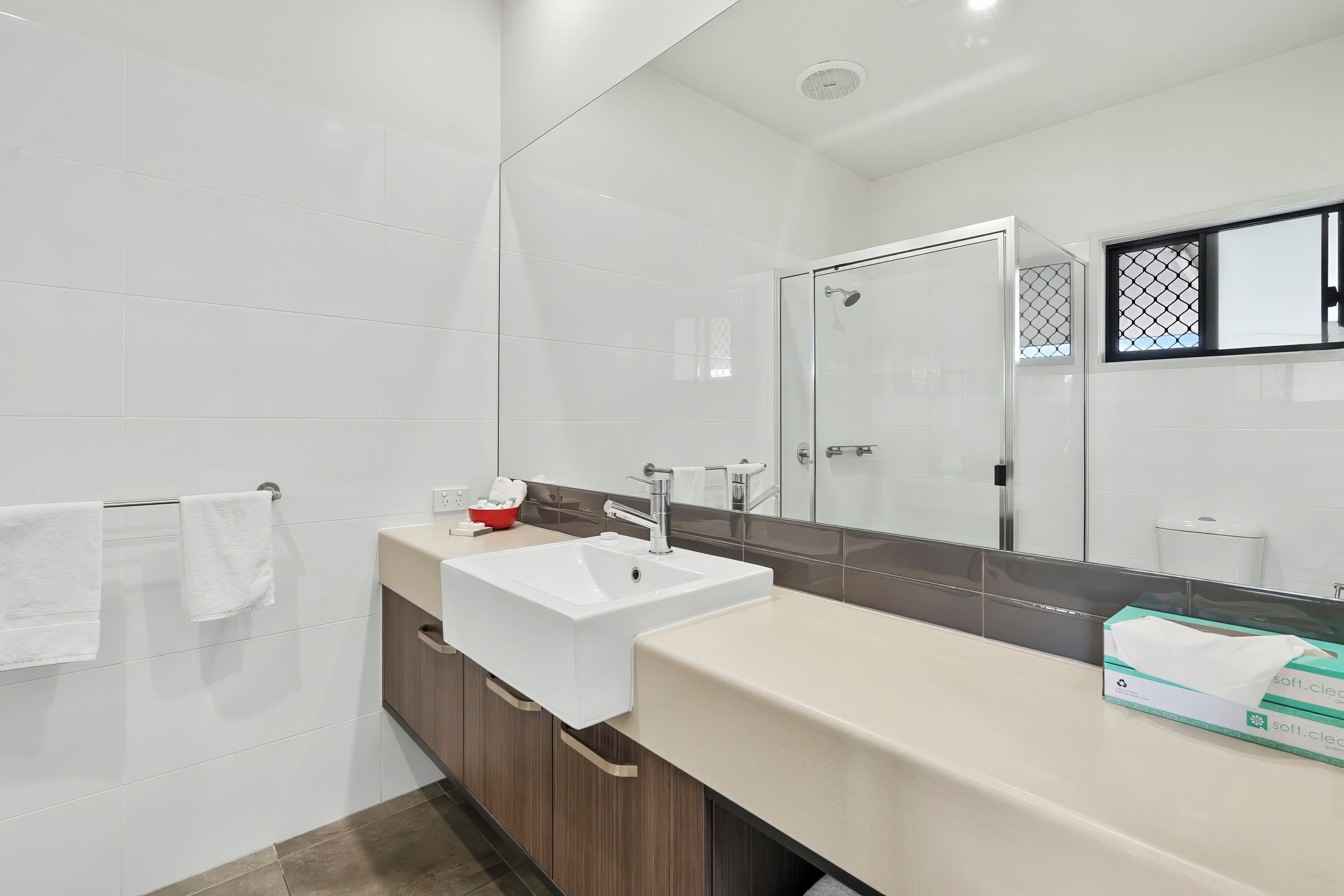Un baño moderno con un lavabo blanco, cabina de ducha con mampara de vidrio y un espejo grande.