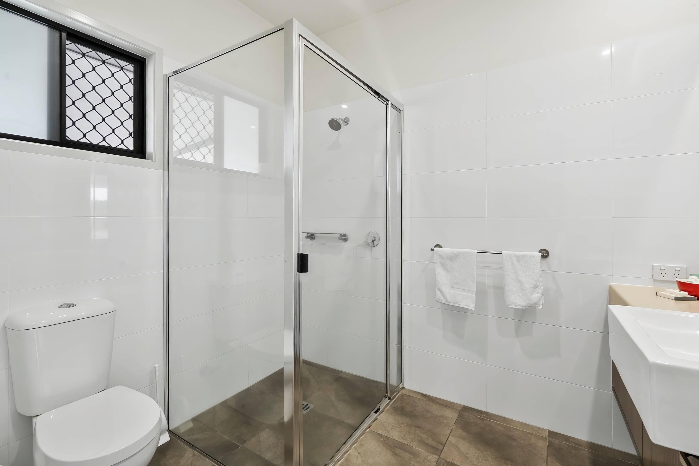 Une salle de bain avec une douche à parois de verre, des toilettes et un lavabo équipé d’un porte-serviettes.