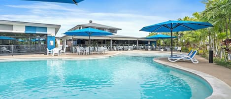 A swimming pool with lounge chairs and umbrellas, surrounded by a building with outdoor seating.