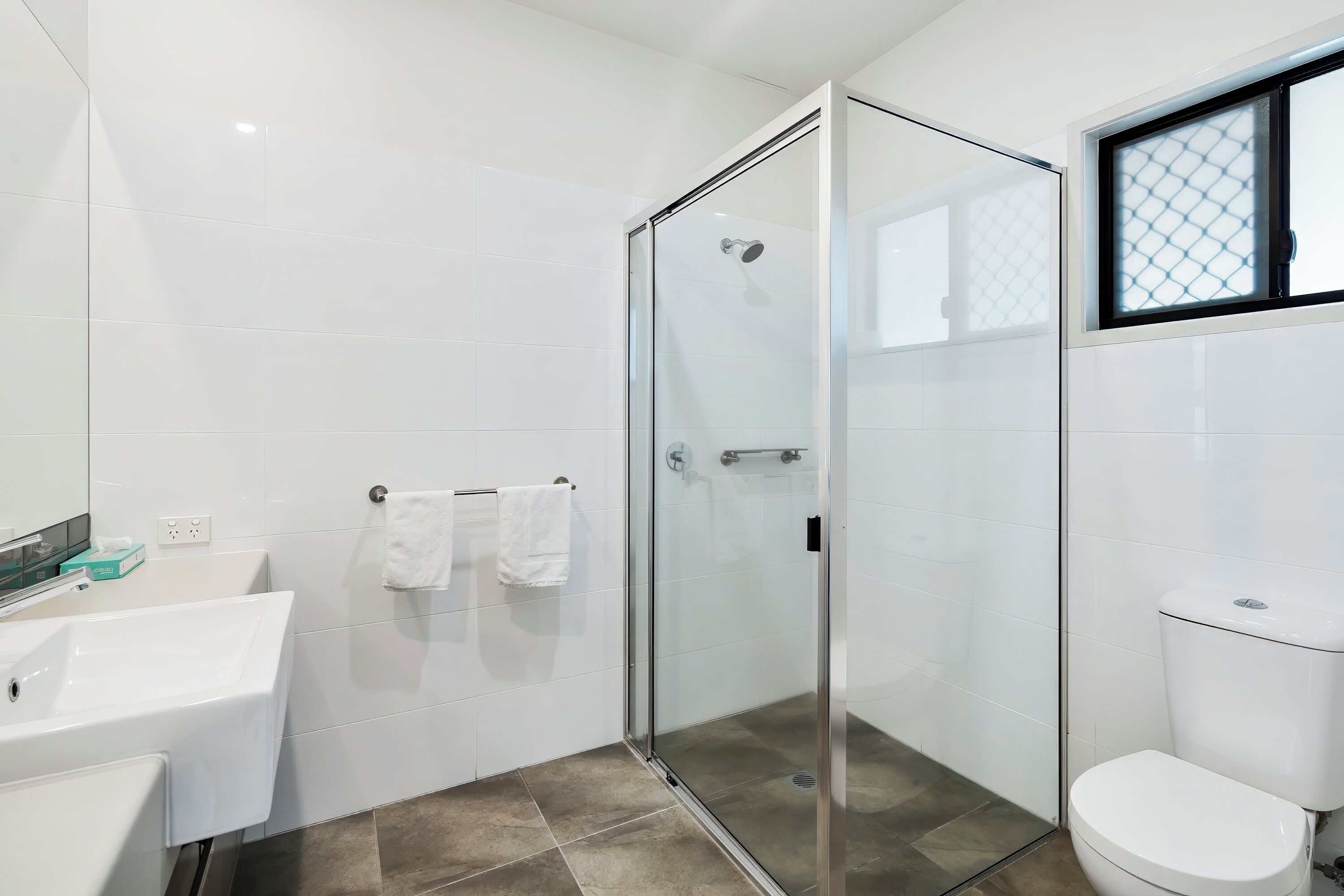 A modern bathroom with a glass shower enclosure, a white sink, and a toilet.