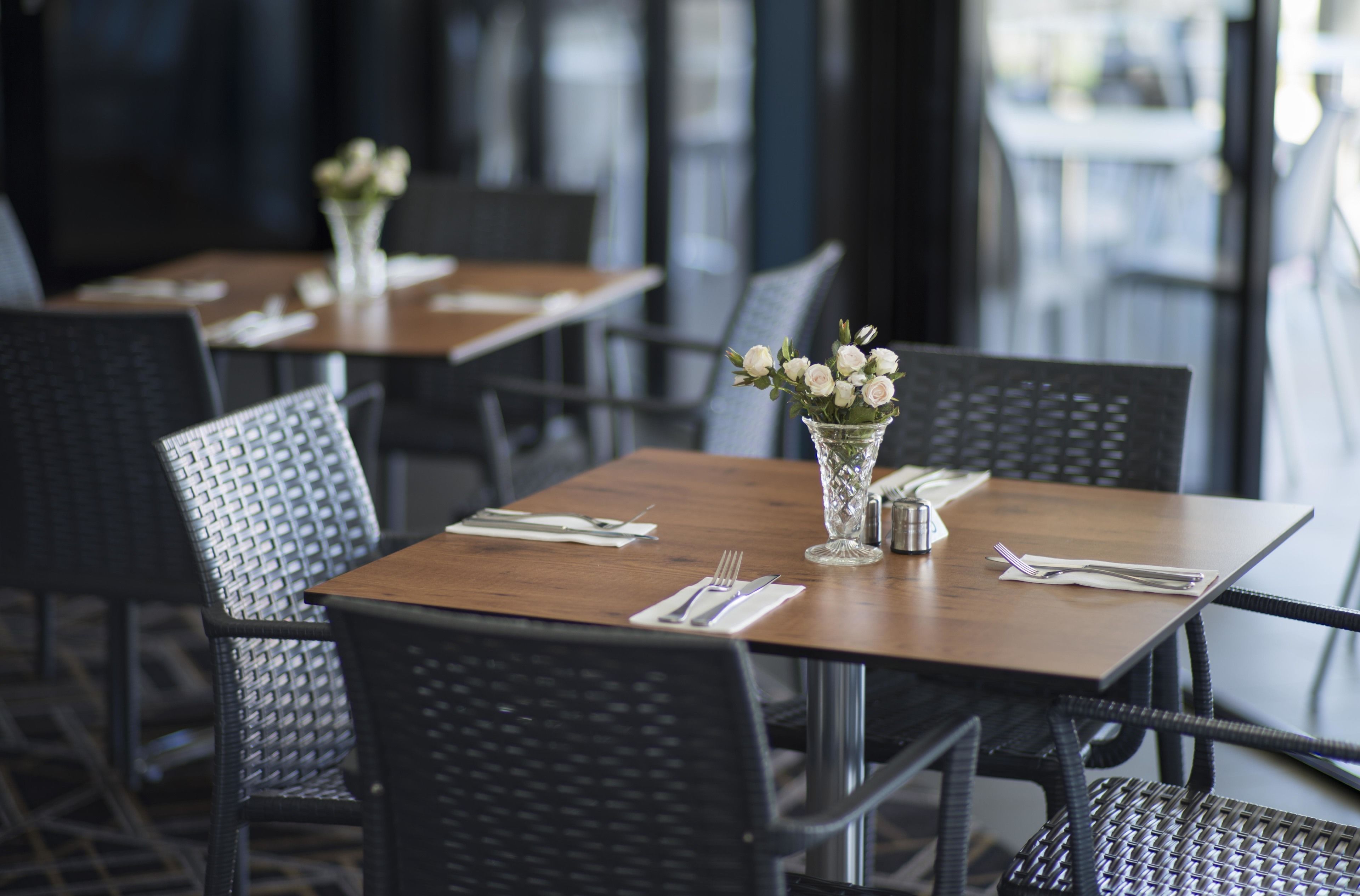Un restaurante con mesas de madera y sillas negras, cada una adornada con un jarrón de flores blancas y vajilla impecable.