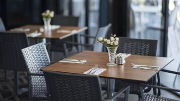 Un restaurante con mesas de madera y sillas negras, cada una adornada con un jarrón de flores blancas y vajilla impecable.