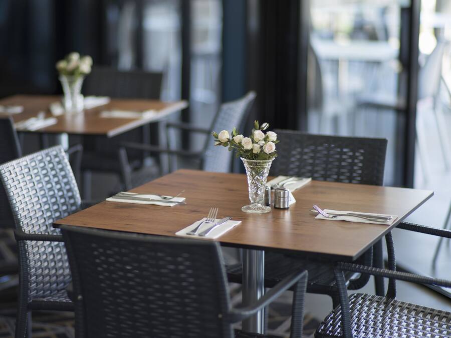 Un restaurante con mesas de madera y sillas negras, cada una adornada con un jarrón de flores blancas y vajilla impecable.