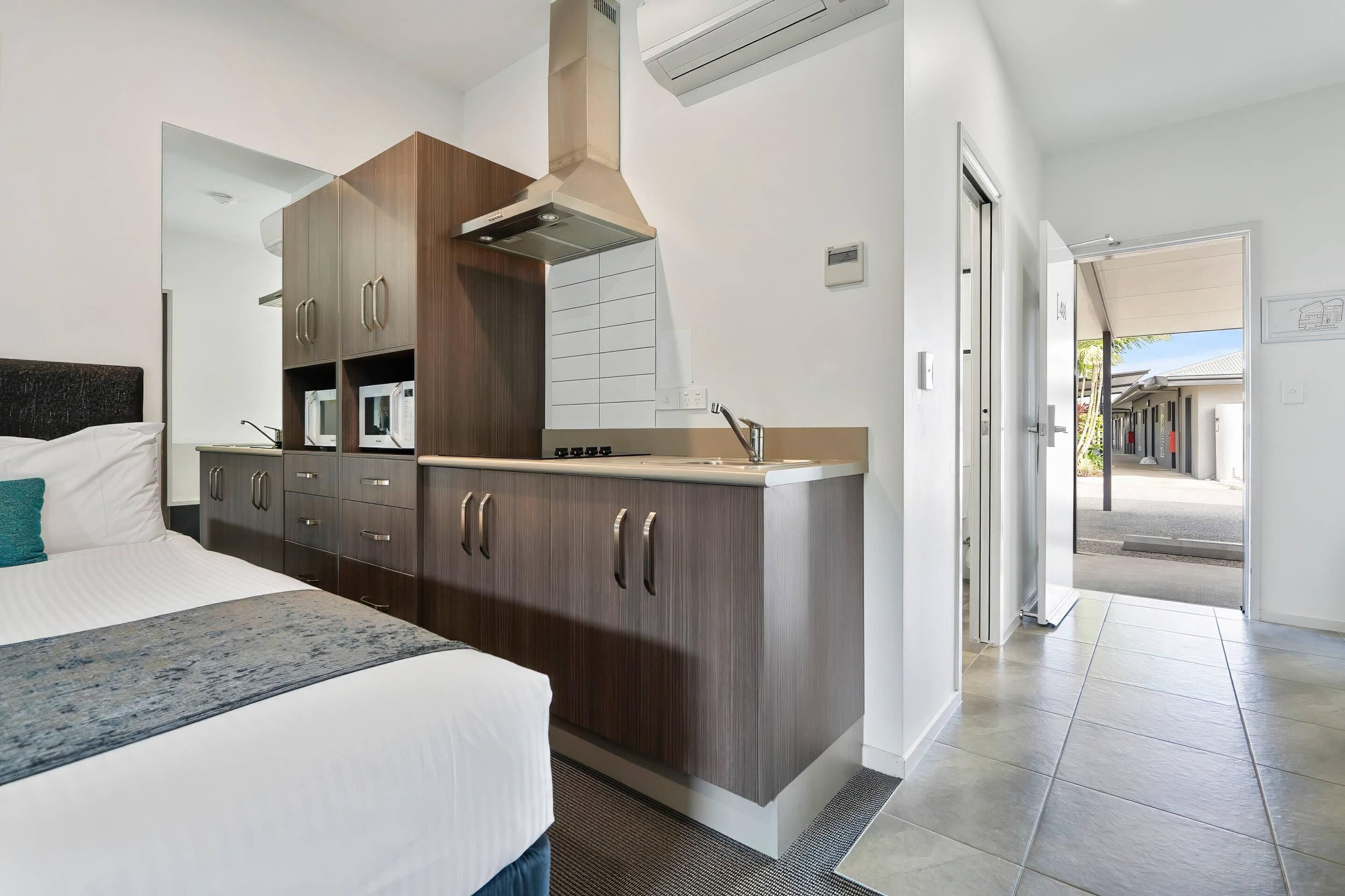 A modern hotel room with a bed, a kitchenette, and a view of the outside.