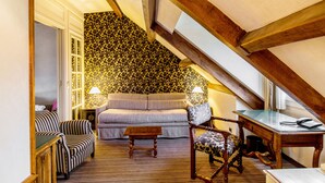 A cozy living room with a sofa, armchairs, a small table, and a desk with a telephone. The room features a patterned wallpaper and wooden beams on the ceiling. - Hôtel Left Bank Saint Germain (Paris)
