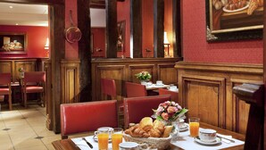 A dining area with red upholstered chairs, a table set with breakfast items, and a painting on the wall. - Hôtel Left Bank Saint Germain (Paris)