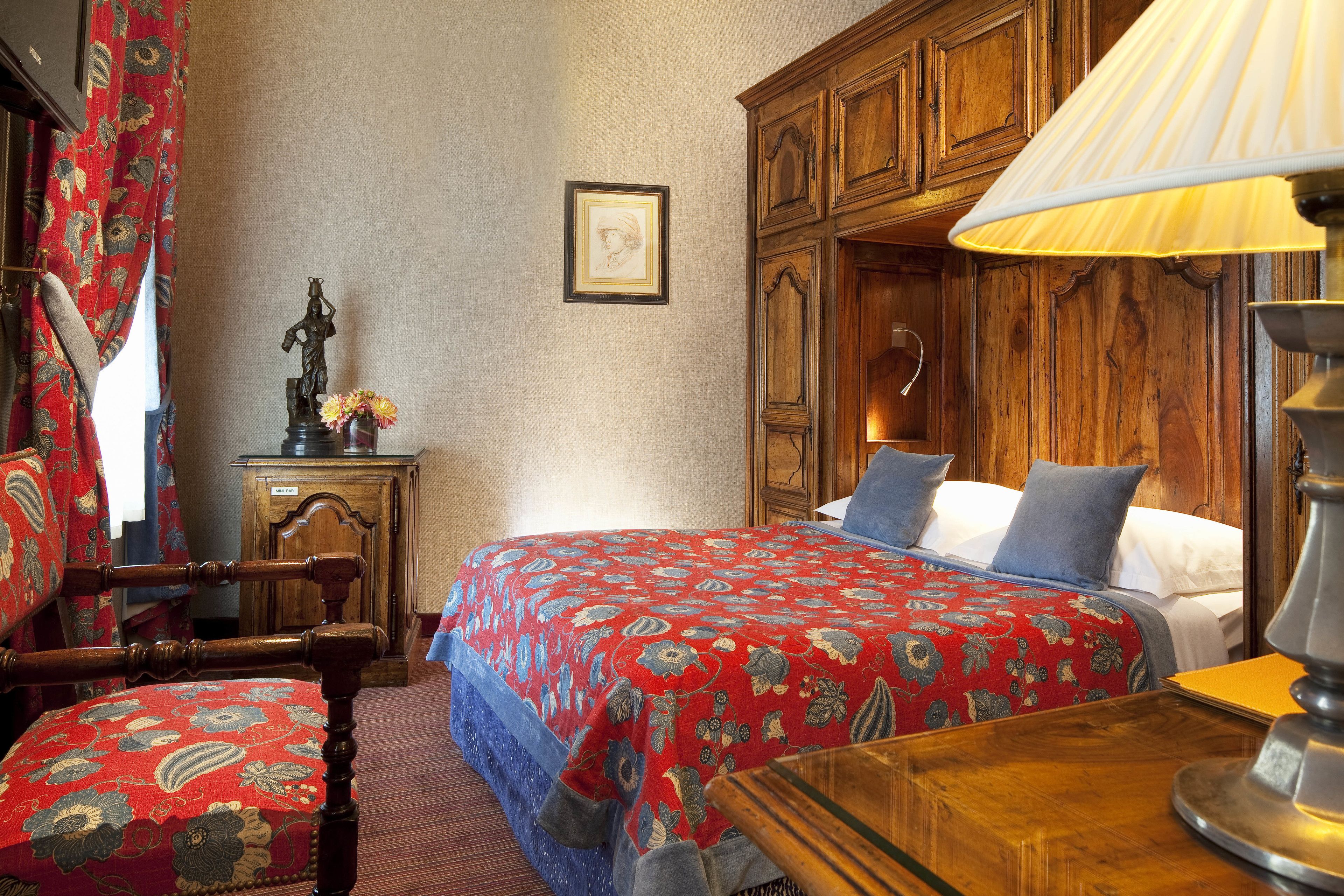 Quarto tradicional com cama de madeira, mesa de cabeceira de madeira, uma cadeira e uma escrivaninha.