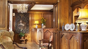 A traditional room with wooden paneling, a chandelier, a floral tapestry, a wooden cabinet with decorative items, and a vintage chair. - Hôtel Left Bank Saint Germain (Paris)