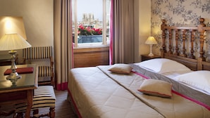 A hotel room with a large bed, a small table with a lamp, a chair, and a view of a building through a window. - Hôtel Left Bank Saint Germain (Paris)