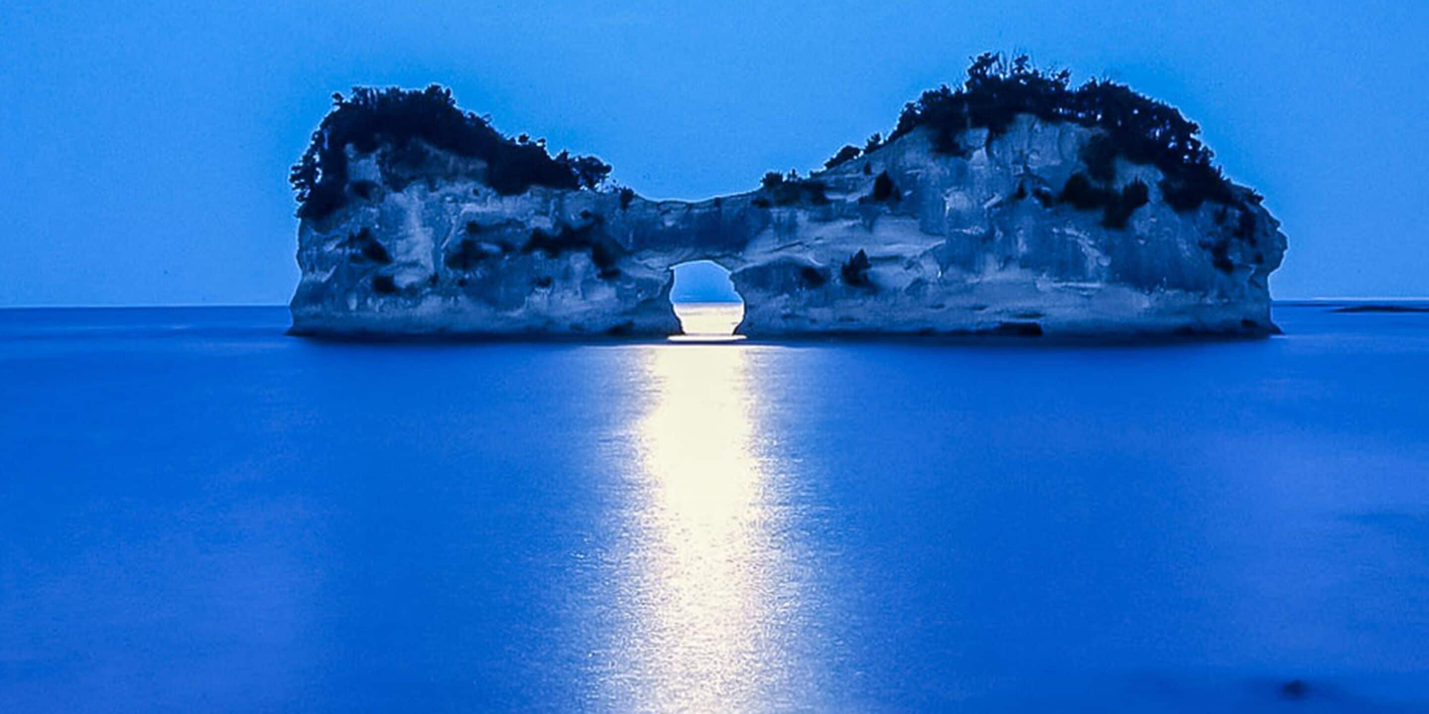 A rock formation with a natural archway in the center, surrounded by calm water.
