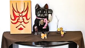 Ein Tisch mit einer kleinen schwarzen Katzenfigur, einem roten und goldenen Gemälde und einer kleinen Personenfigur.
