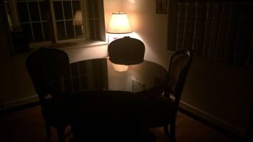 A dimly lit room with a round table and two chairs, a lamp on the table, and a window with blinds.