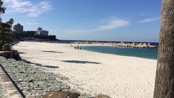 A beach with white sand, clear blue water, and rocky formations.