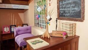 A cozy room with a purple sofa, a wooden desk with a chalkboard, and a decorative tree.
