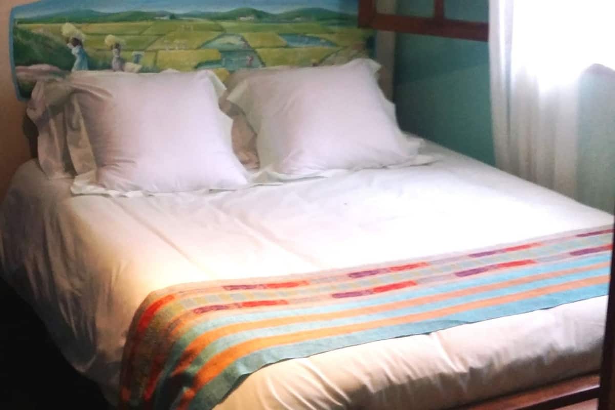 A bed with white bedding and a colorful striped blanket.