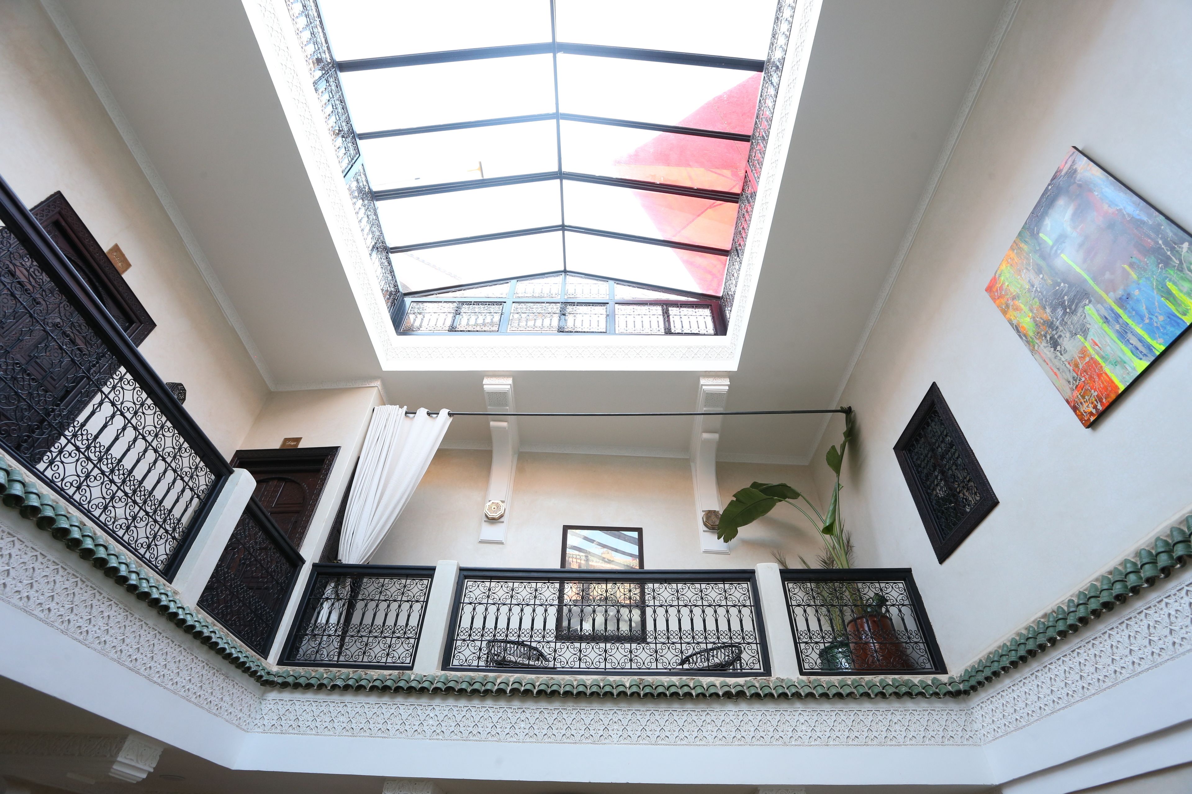 Ein mehrgeschossiges Interieur mit Dachfenster, dekorativen Geländern und einem gerahmten Kunstwerk an der Wand.