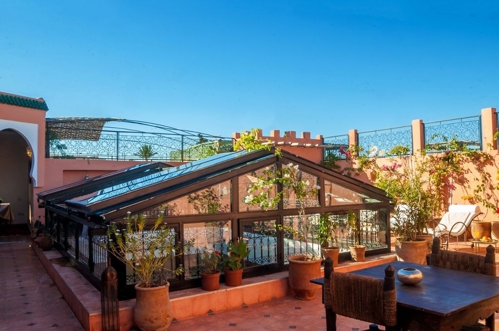 Eine Dachterrasse mit einem Glashaus, Kübelpflanzen und Gartenmöbeln.