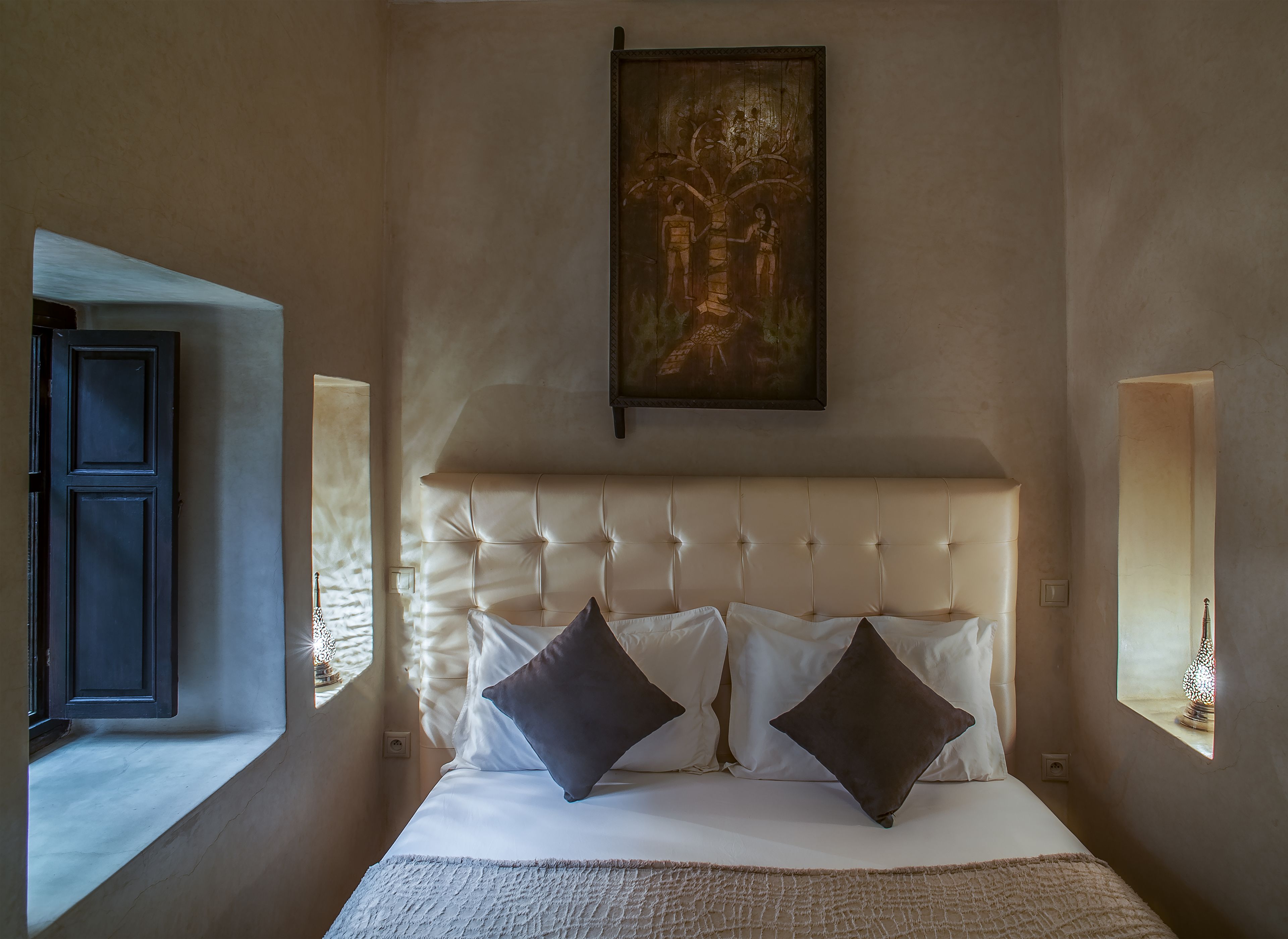 Una camera da letto con un letto grande, una testiera, due lampade sui comodini e un quadro appeso al muro.