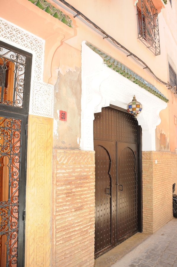 A traditional Moroccan gate with intricate metalwork, a white decorative archway, and a tiled roof.