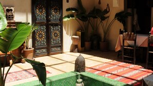 Un patio con suelo de baldosas, una fuente, plantas en macetas y un puerta grande con diseños intrincados.