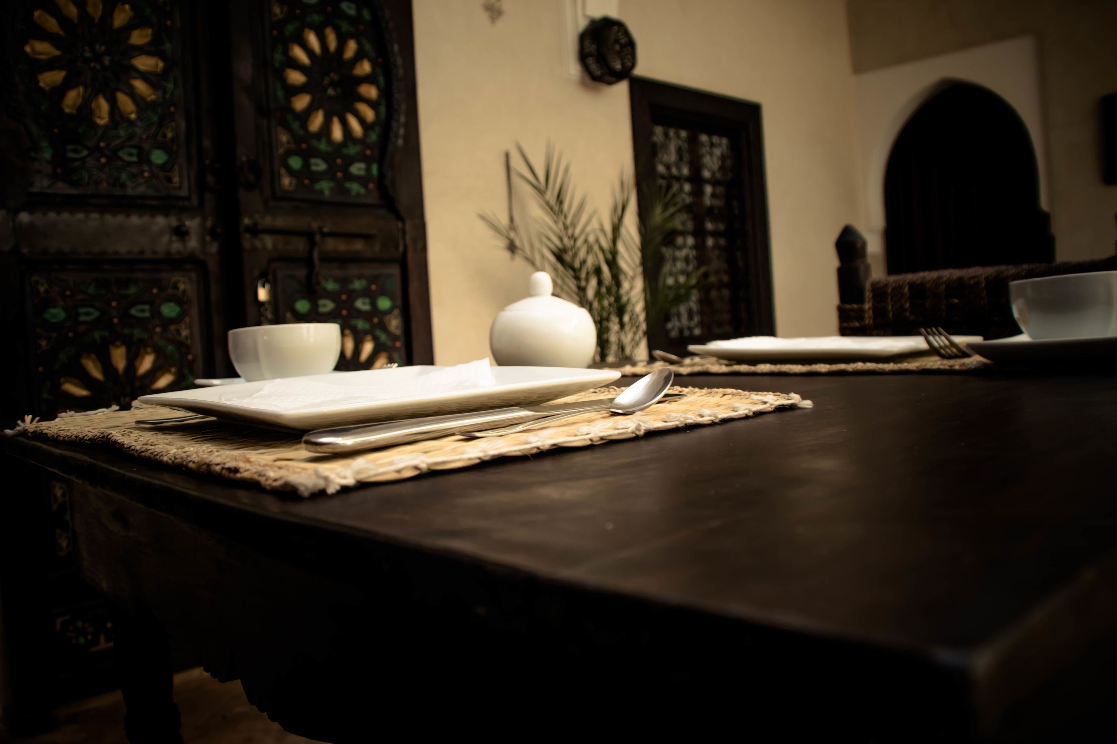 A dining table set with white plates, a spoon, and a pitcher, with a woven placemat.
